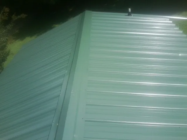 New green metal panels meeting at the ridge of a roof — Flat Roof Repair work by our crew in Mentor