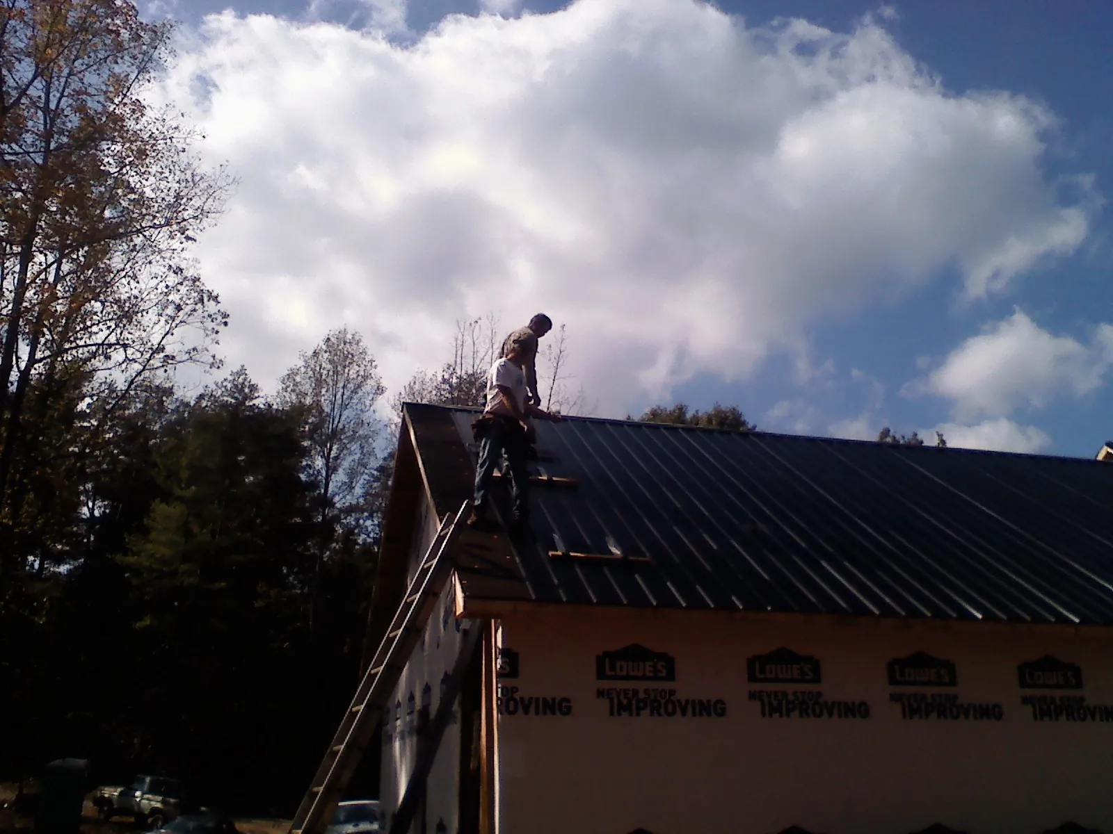 Roofer fastening dark metal panels high against a cloudy sky, from a Roof Inspection job in Mentor